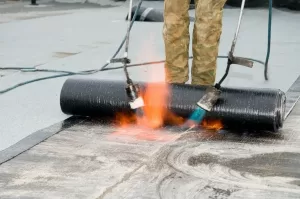Worker installing roofing felt using torches on a flat roof.
